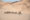 Aerial shot of a herd of around 15 desert adapted elephants trudging through sandy dunes.