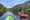 two people in individual kayak boats, on a river surrounded by lush green shrubs and trees, under blue skies.