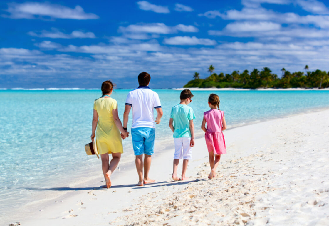 family walking on a stunning white sand beach surrounded by crystal clear ocean