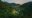 Aerial view of El Silencio Lodge & Spa in Costa Rica, nestled in a lush green valley surrounded by forested mountains. The eco-lodge’s wooden rooftops, pathways, and gardens blend seamlessly into the cloud forest landscape beneath a soft morning sky.