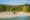 view looking onto a beach lined with sun loungers and umbrellas and behind that thick palm tree forest and to the right a building with a pointed roof peeks through the trees with a platform that comes out on to the sand