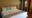 a double bedroom featuring double bed with lace throw, yellow and green cushions, small wooden wardrobe with shelves and two dressing gowns