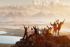 Big group of people having fun in success pose with raised arms on mountain top against sunset lakes and mountains. Travel, adventure or expedition concept