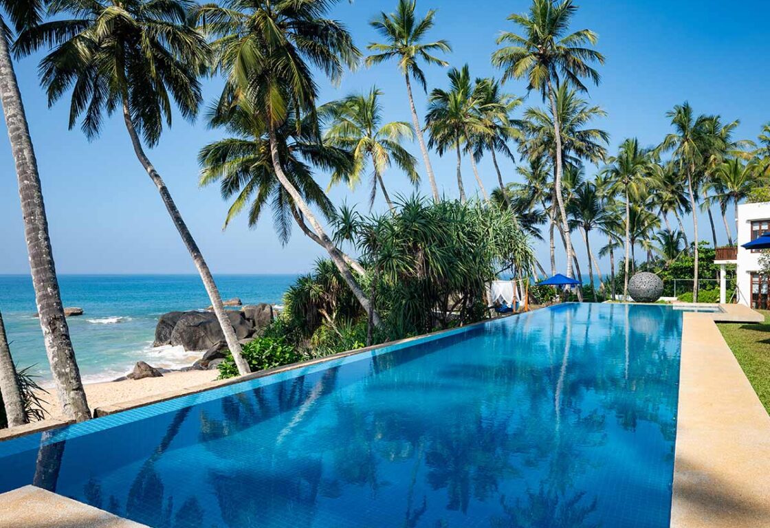 Infinity pool overlooking a palm-lined beach and the Indian Ocean at Kumu Beach, Sri Lanka.