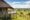 The exterior of a thatched safari tent on a raised wooden deck with a dry-stone base wall, its private veranda overlooking a sweeping panorama of the Serengeti plains and the winding Mara River far below