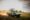 A dark green safari Land Cruiser with an open pop-up roof hatch and guests standing up through it kicks up a trail of dust as it drives across the Serengeti plains at golden hour, with warm backlit sunlight streaming across the grassland.