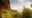 A view from one safari tent's private deck looking along the ridge toward two neighbouring thatched accommodation units, their rooflines emerging above a lush green canopy of trees, with a low bank of cloud sitting on the horizon under a soft blue sky