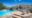 A freeform swimming pool on a layered sandstone terrace built against a dramatic granite kopje boulder, with modern grey outdoor lounge furniture tucked into a natural rock alcove, two large planted pots and a vivid blue sky above.