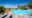 A freeform infinity-style swimming pool with curved entry steps on a sandstone terrace, flanked by grey sun loungers, with an uninterrupted view across the vast flat Serengeti plains under a vivid blue sky