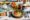 a table set with plates of food with avocado, eggs, watermelon and tomatoes, cup of coffee and cuttlery