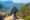 Girl sitting on rock edge with back to photo looking out over a huge green canyon and blue lake below.