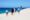Six people walking away from the camera along a stunning white sand dune with blue ocean in the background.